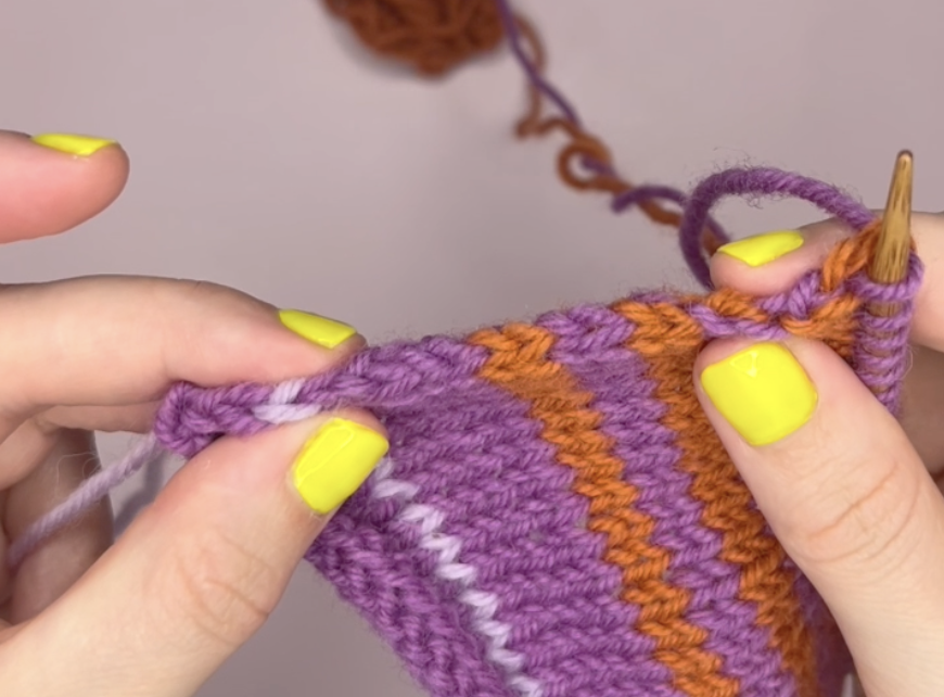 person with yellow nail polish holding a piece of knitted fabric with orange and purple stripes