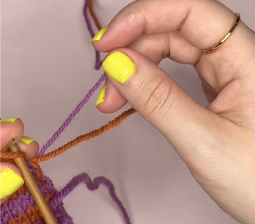 holding two different colours of yarn in one hand, one orange and one purple